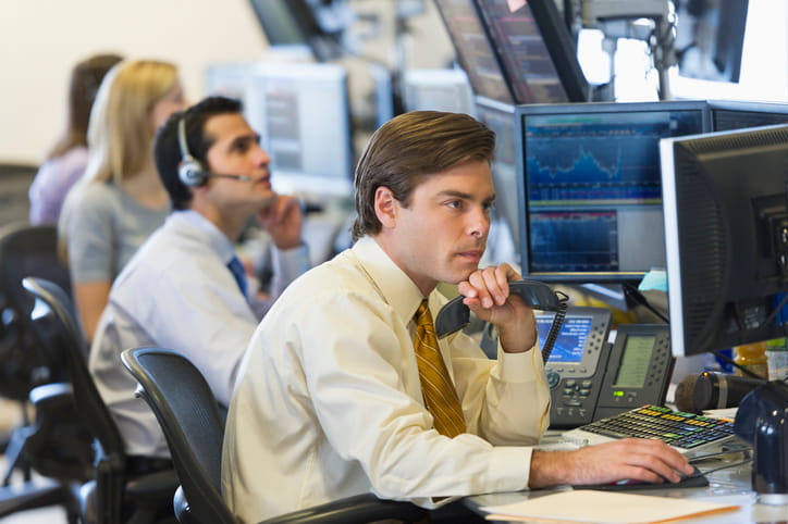 A quantitative analyst on the phone reviewing disability insurance coverage options across multi-monitor trading desk screens