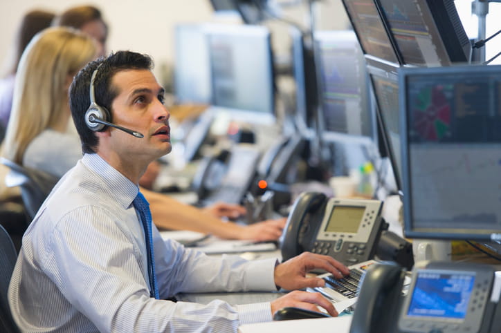 Asset manager on a phone headset reviewing disability insurance coverage options across multiple market-data screens