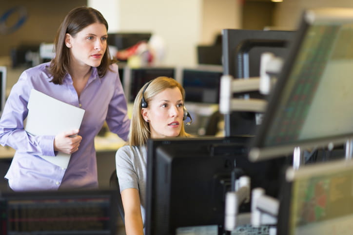 Two portfolio managers reviewing disability insurance coverage options on a multi-monitor trading desk