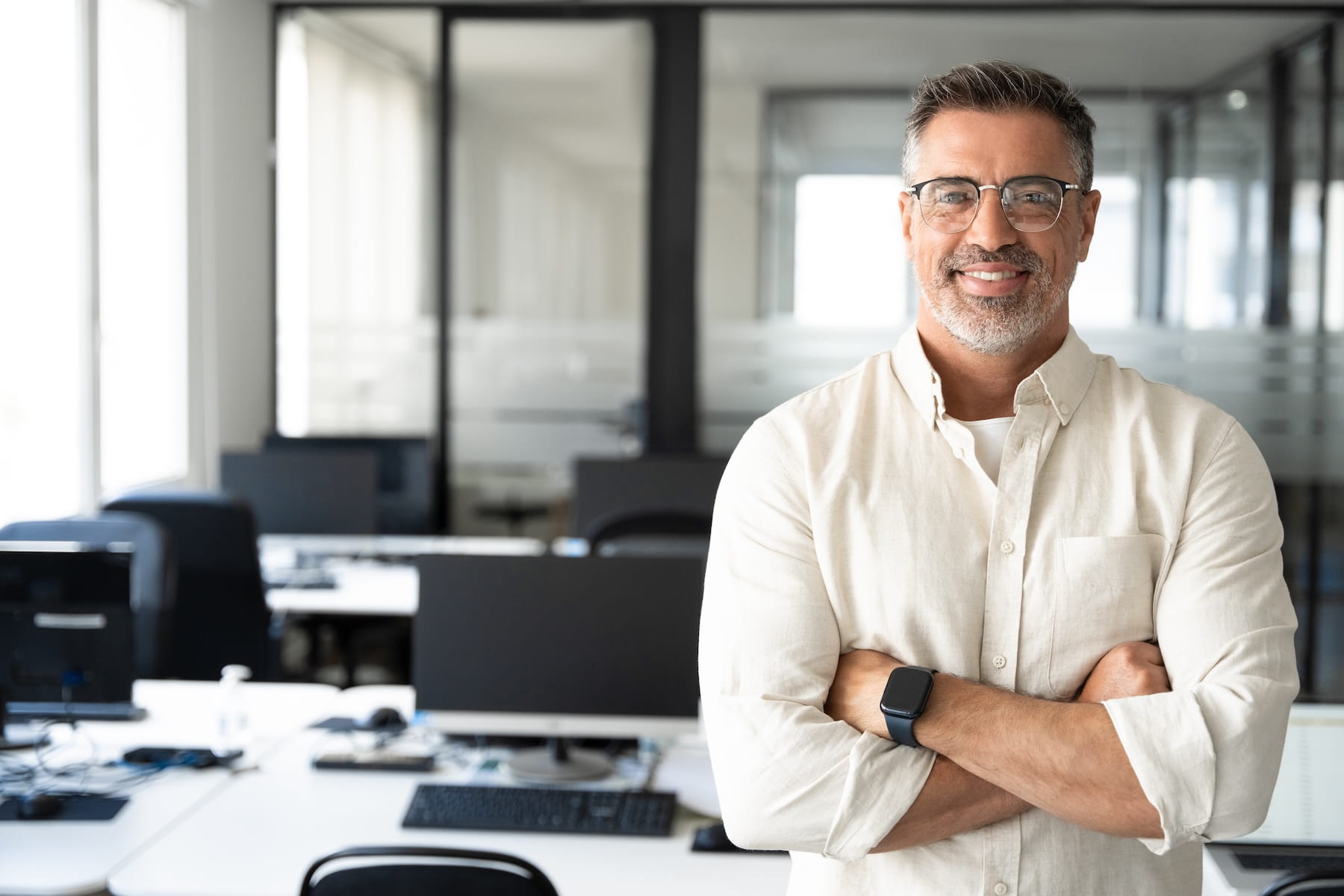 Executive standing arms crossed in a modern office, the key person whose disability would cost the business its expertise and revenue, the risk key person disability insurance from Guardian, Principal Financial Group, MassMutual, or The Standard is designed to fund